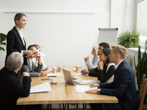 Successful female boss leading team meeting talking to multiracial employees, woman executive leader discussing work results presenting contract report to diverse partners at company group briefing