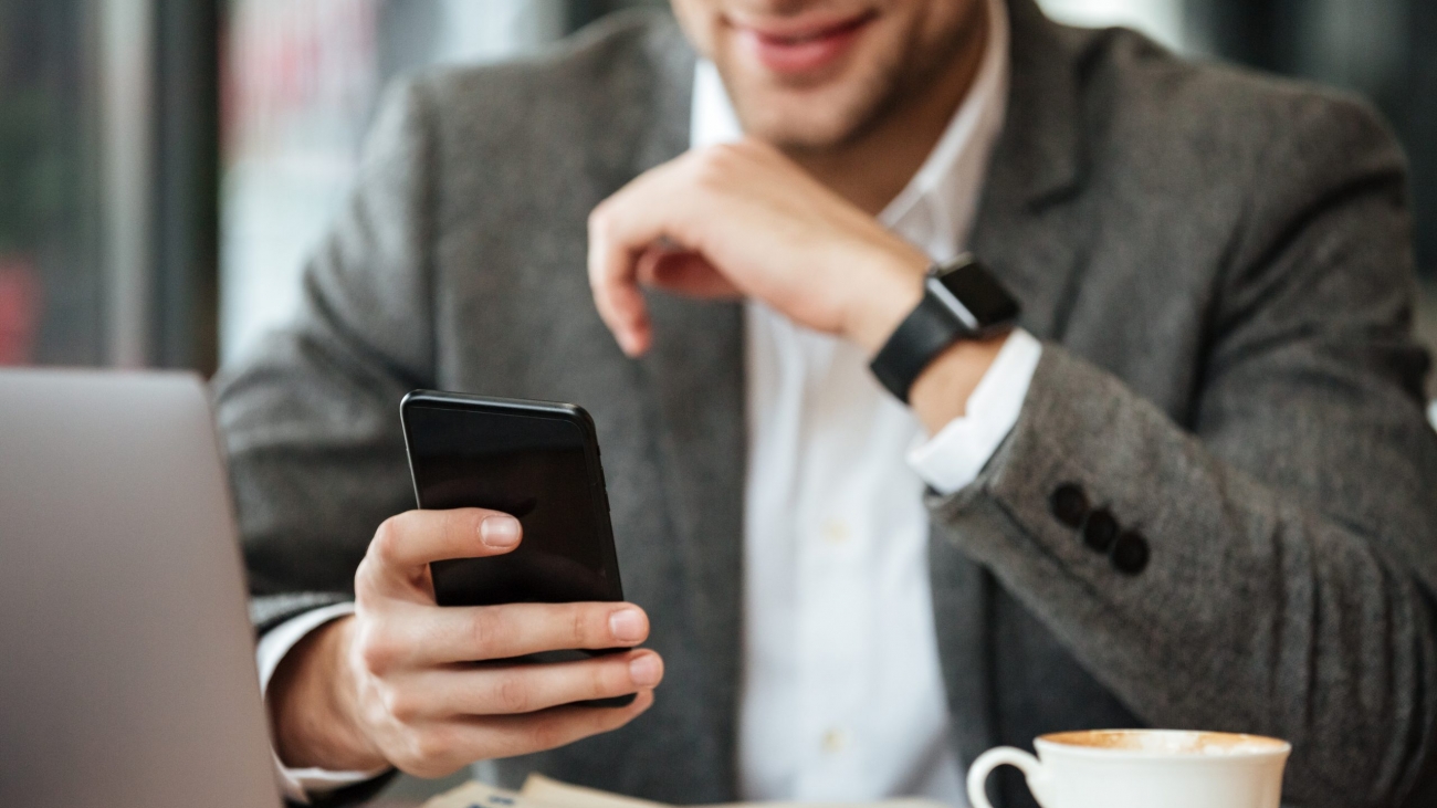 Cropped image of happy business man sitting by the table in cafe and using smartphone