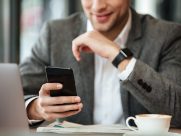 Cropped image of happy business man sitting by the table in cafe and using smartphone